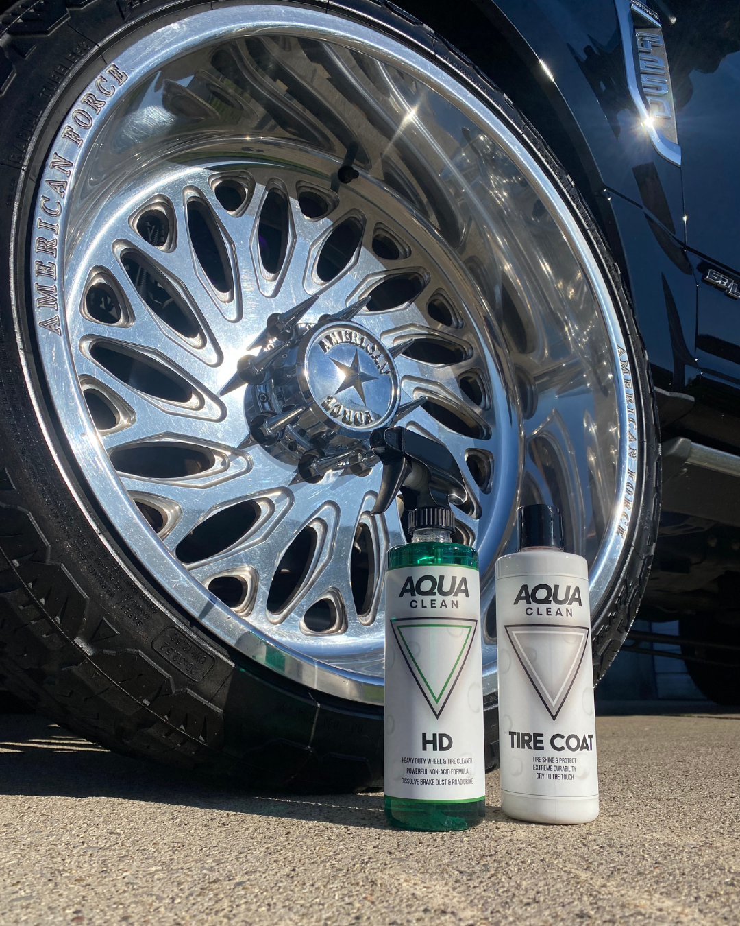 Two AquaClean product bottles displayed in front of polished chrome car wheel